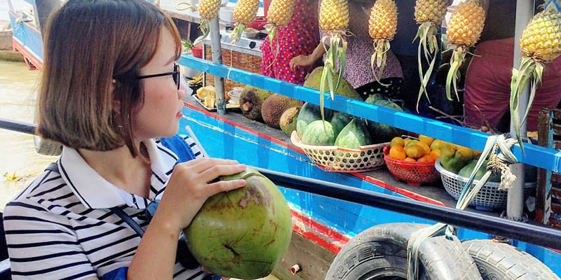 Du khách thưởng thức nước dừa tươi ngay trên thuyền tại chợ nổi Cái Bè. 